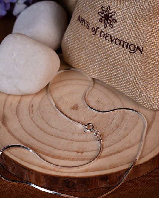 Silver necklace on a wooden surface with 'Arts of Devotion' packaging.